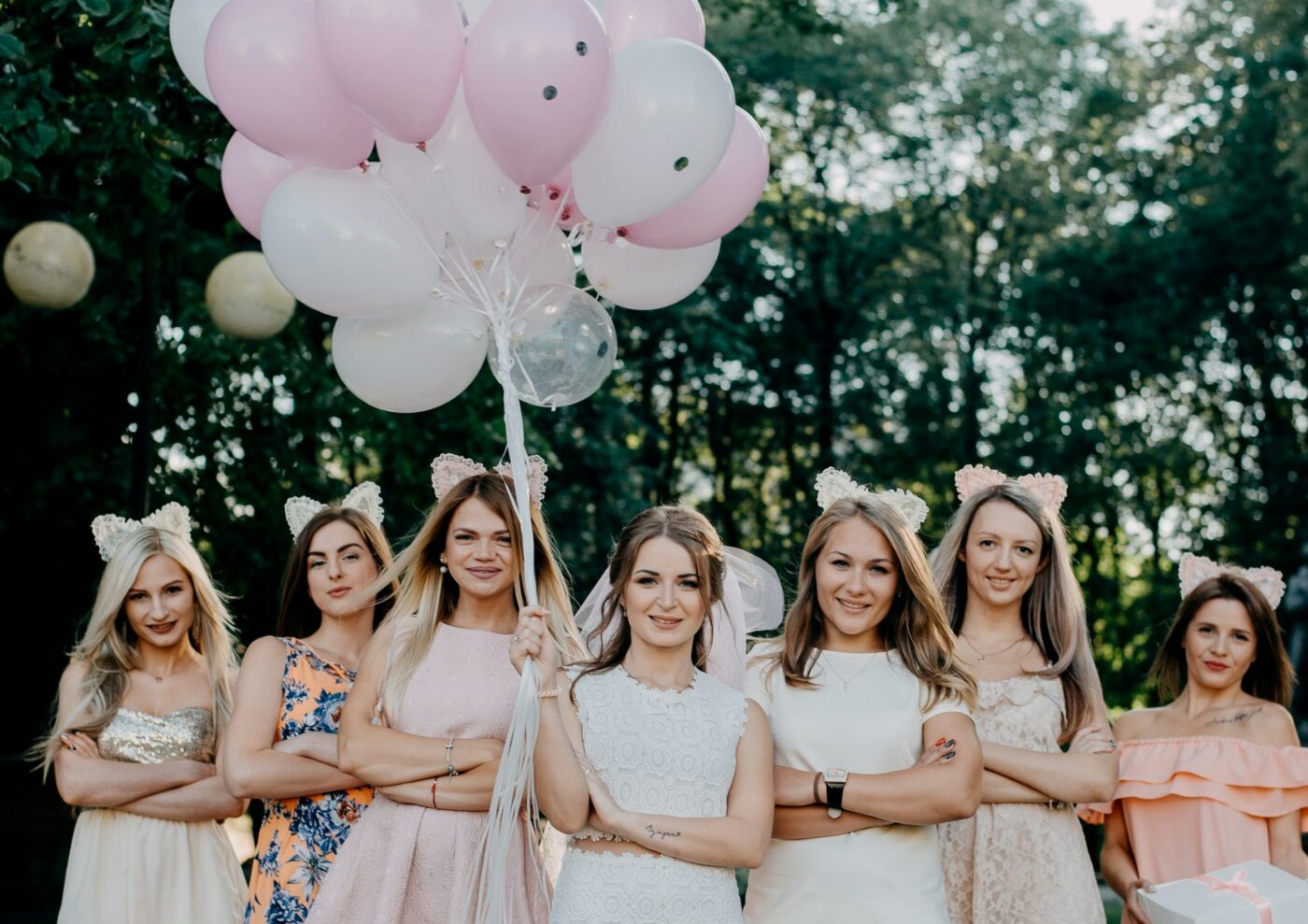 Bride holding balloons in the middle of her bridesmaids in front of some trees