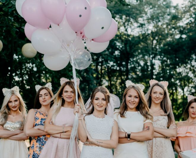 Bride holding balloons in the middle of her bridesmaids in front of some trees